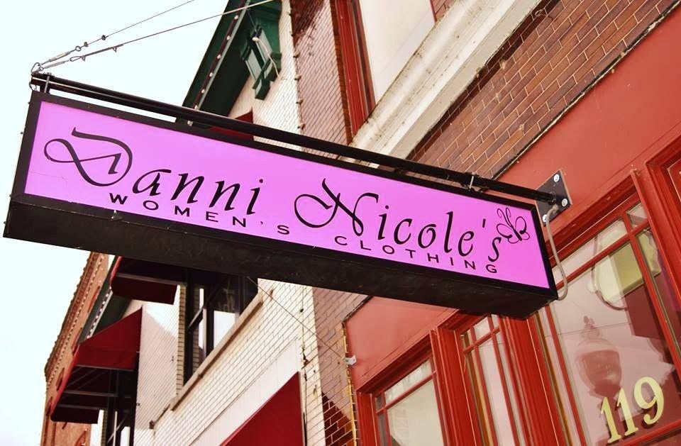 The magenta hanging sign reading Danni Nicole's in black script over the words women's clothing, mounted on a bracket against a brick wall